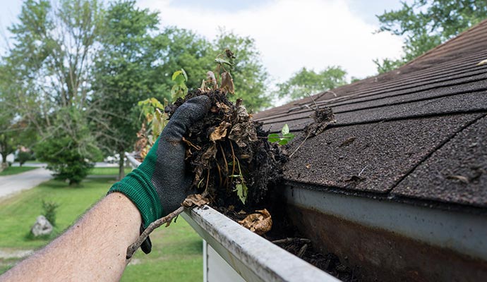 A person cleaning gutter wearing gloves