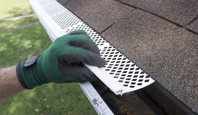 A person clearing wet roofing material from gutter