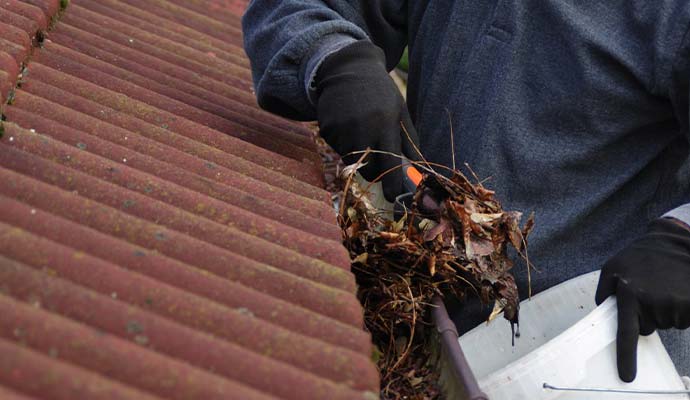 A person removing debris from a clogged gutter