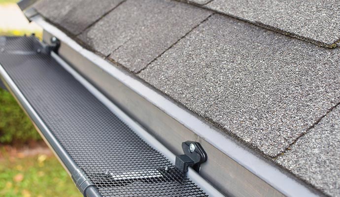 A close-up view of a black mesh gutter guard system installed on a residential roof with grey shingles