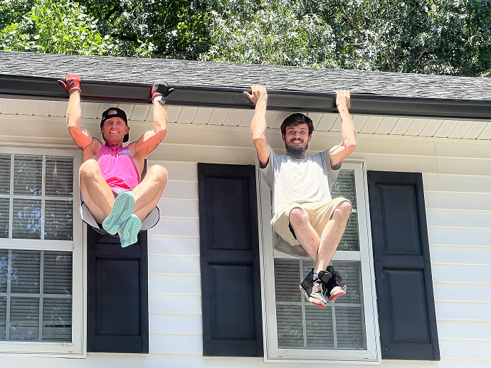 Two professionals hanging from a home's gutter during a strength demonstration