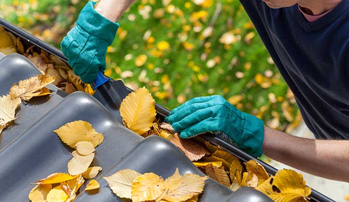 Technician using a scoop to clear autumn leaves from a seasonal gutter