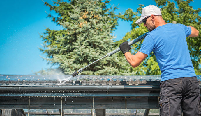 Technician clearing roof  gutter channels with high pressure water
