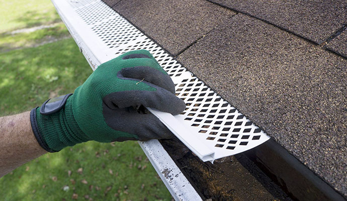 Technician installing a mesh gutter guard on a roof gutter