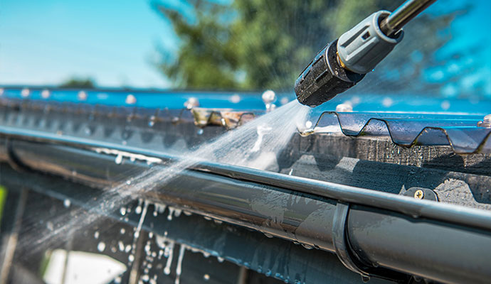 Water spraying from a nozzle to soft wash a roof gutter