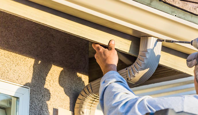 A professional installing a downspout beneath a roof gutter to direct rainwater away from the home’s foundation.