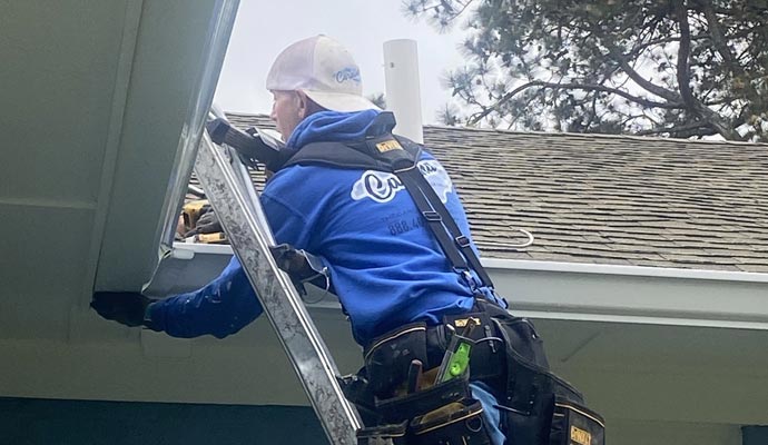 A professional installer working on a home roofline to securely install a long-lasting gutter system.