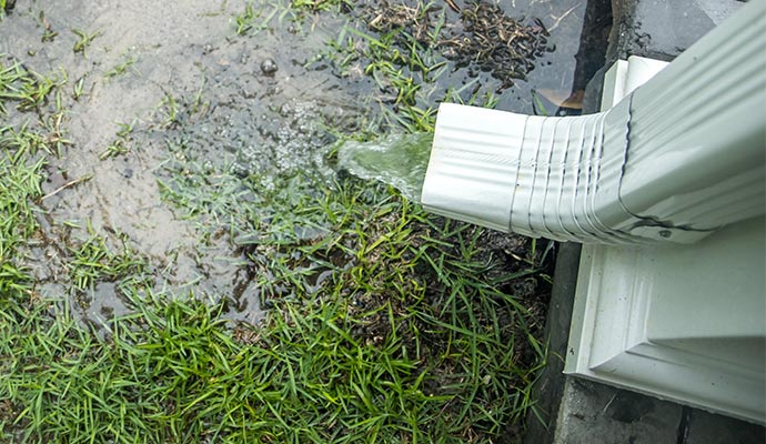 Water flowing from a downspout and pooling near a home’s foundation, indicating a drainage issue.