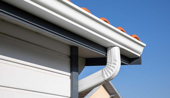 House roof with white rain gutter and downspout